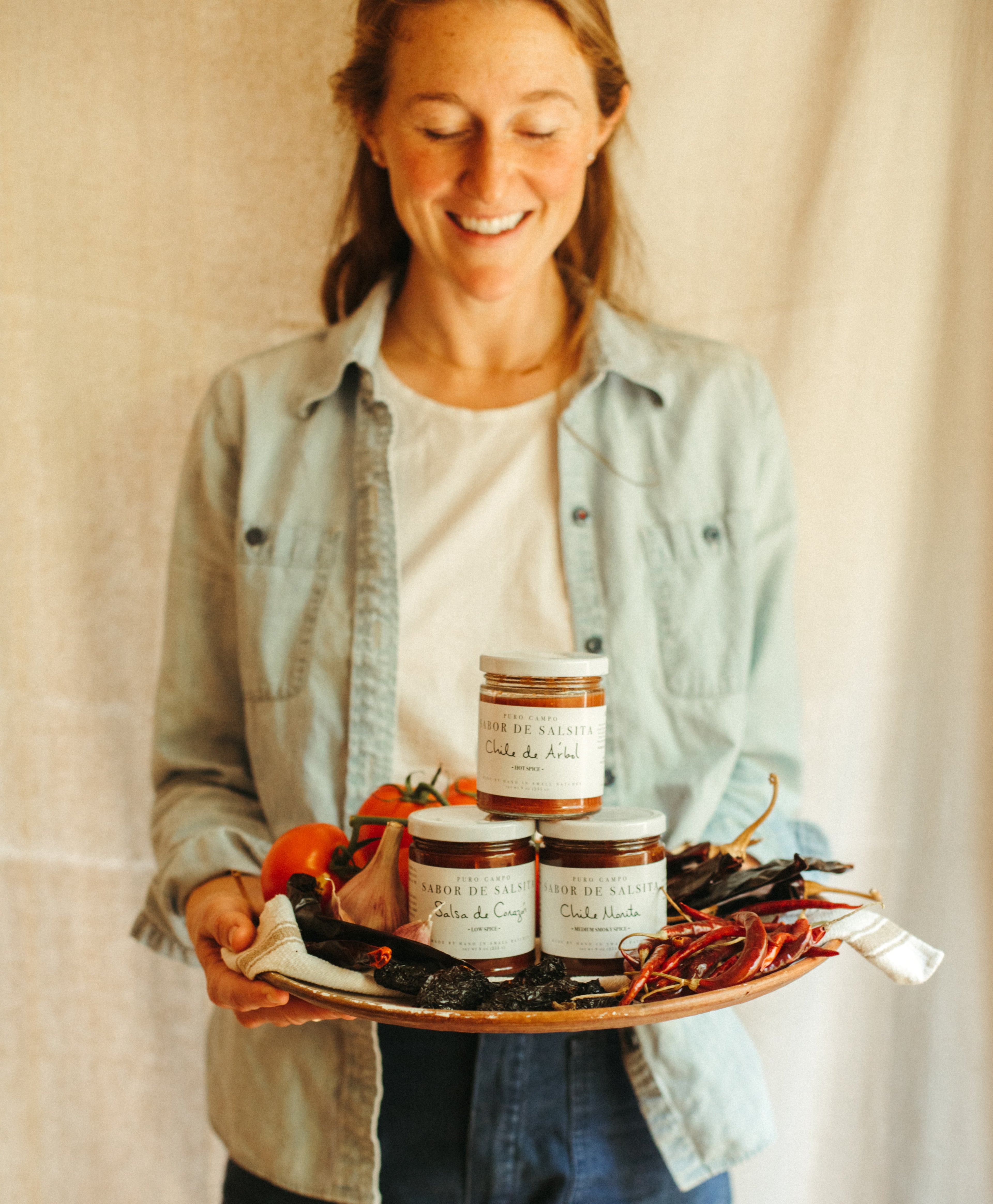 Woman holding a tray with jars and peppers against a neutral background