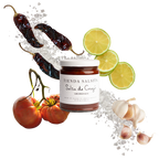 Jar of 'Tienda Salsita' salsa surrounded by chili peppers, tomatoes, and limes on a white background