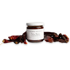 Jar of Thenda Salsita salsa with dried red chilies on a white background