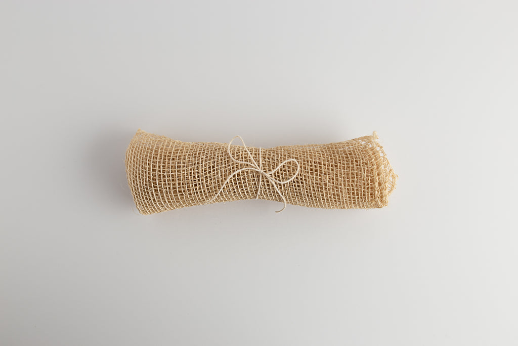 A rolled up beige agave washcloth tied with string, on a white background.
