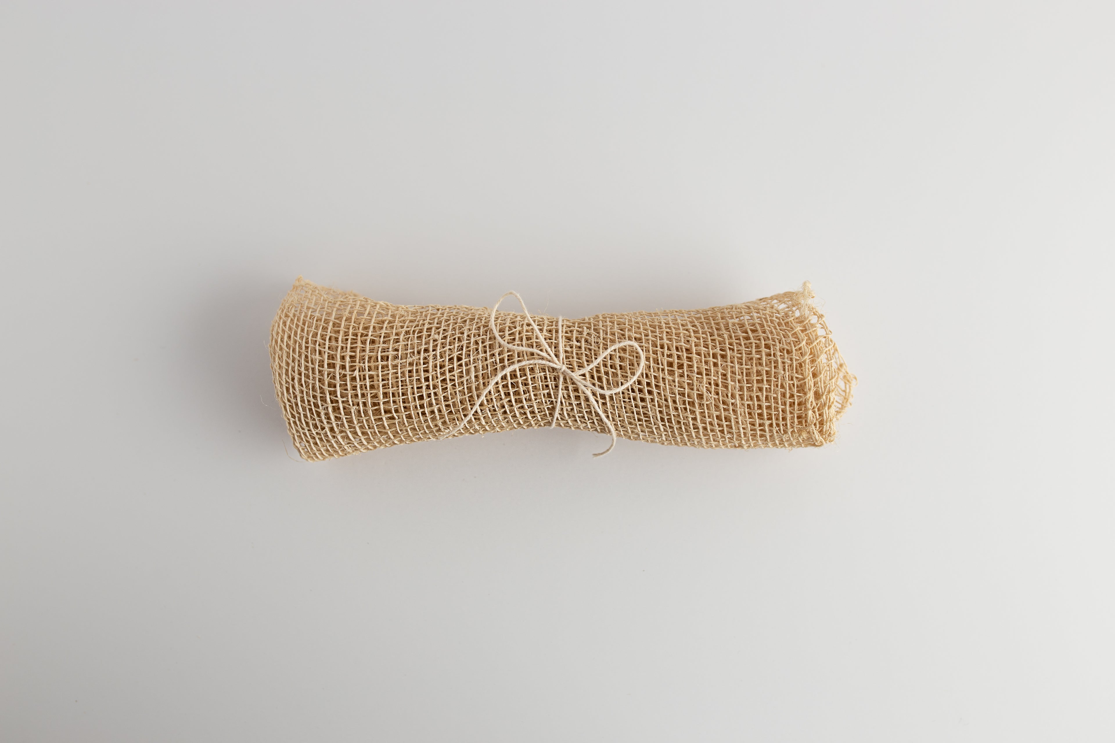 A rolled up beige agave washcloth tied with string, on a white background.